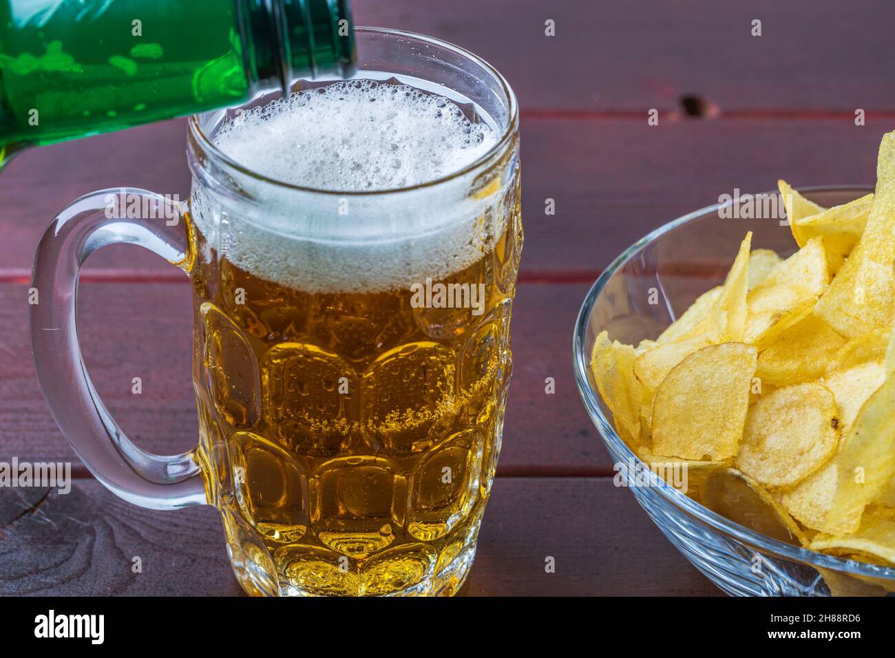 View of pouring beer into a mug and plates with potato chips isolated on wooden background. Stock Photo