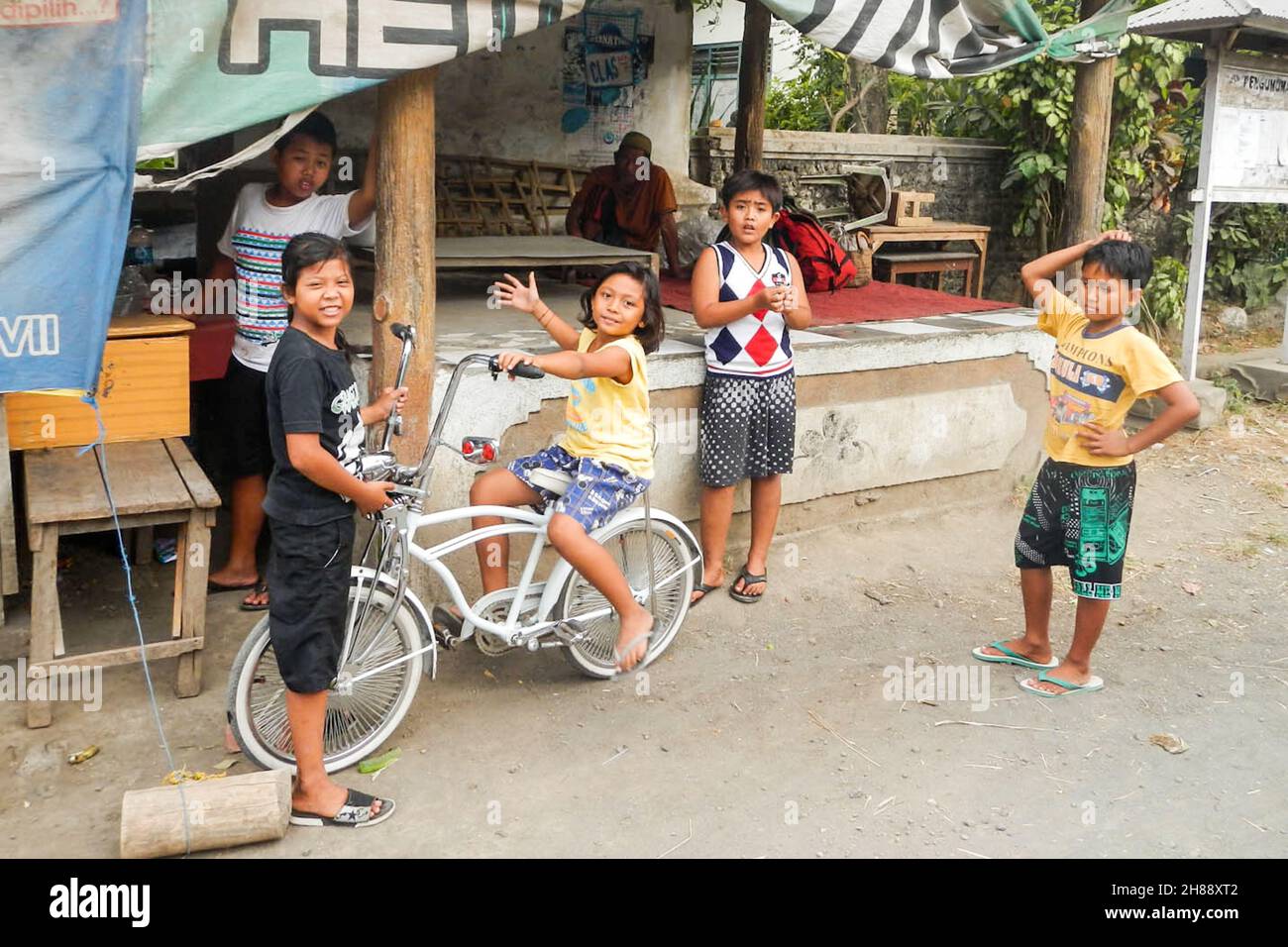 Young Asian kids playing together, one girl is sitting on a bike. Group of Indonesian children. Stock Photo