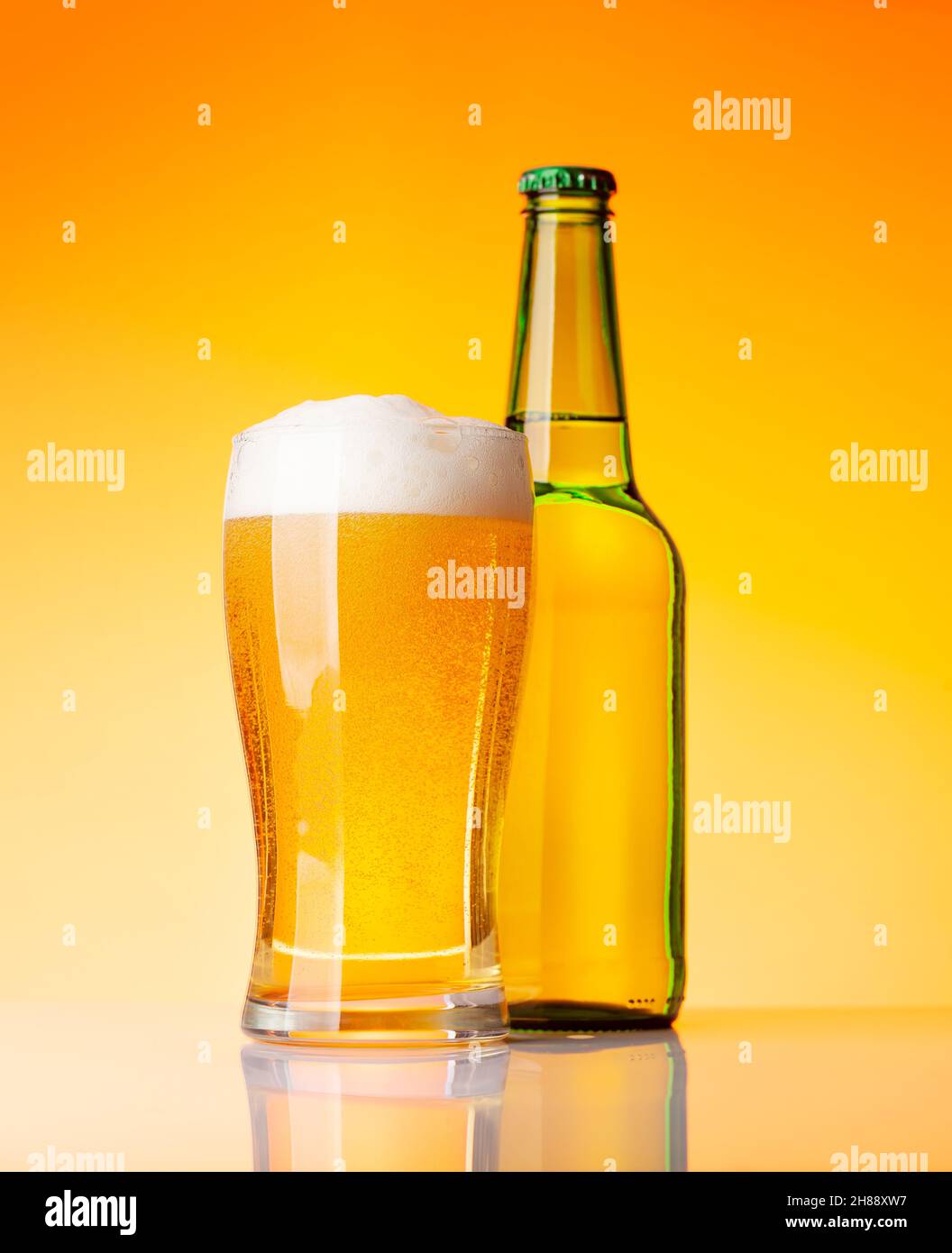 Beer bottle and glass with lager beer in front of yellow background