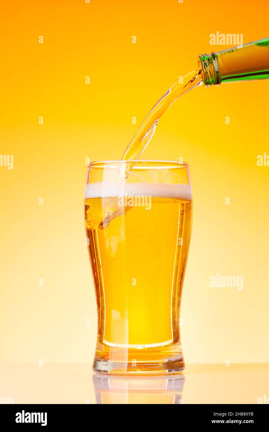 Beer pouring from bottle into glass in front of yellow background. Studio shot Stock Photo Alamy