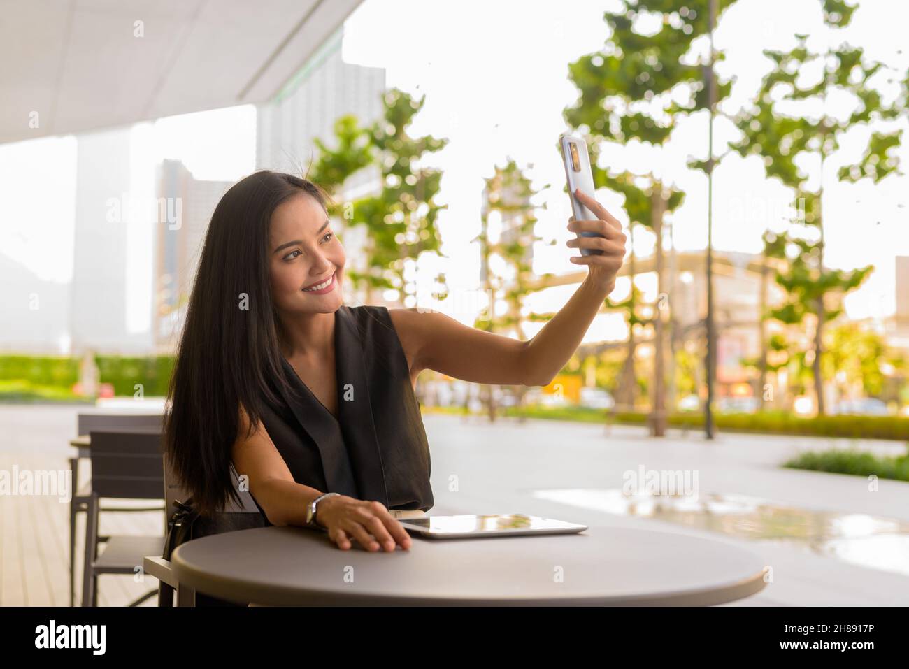 Portrait of beautiful Asian woman sitting outdoors at coffee shop restaurant during summer Stock Photo