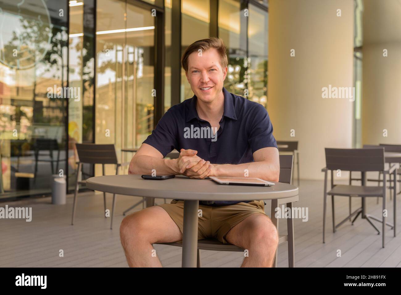 Happy young man sitting outdoors at coffee shop during summer horizontal shot Stock Photo