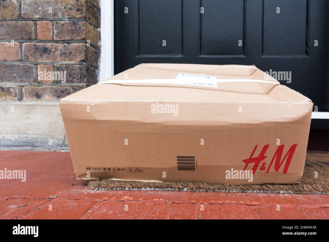 Fashion label H&M sends parcels in cardboard box left in front of a house front door. Stock Photo