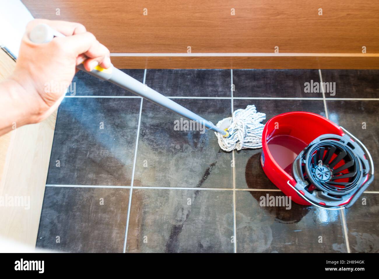 Adult asian male mopping tiled floor with a rope mop and a mop bucket Stock Photo