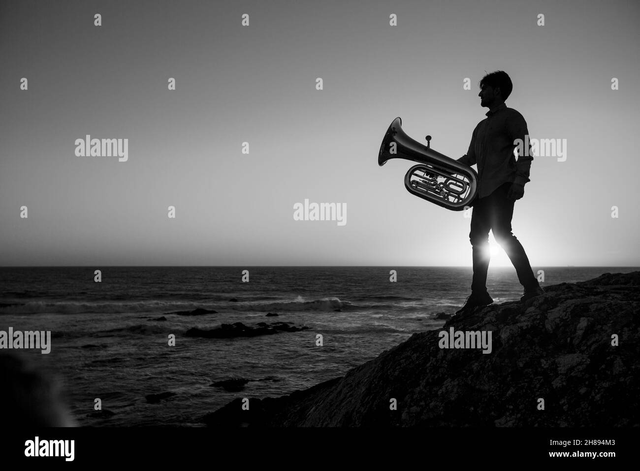 Silhouette of a man with a trumpet by the ocean during sunset. Black and white photo. Stock Photo