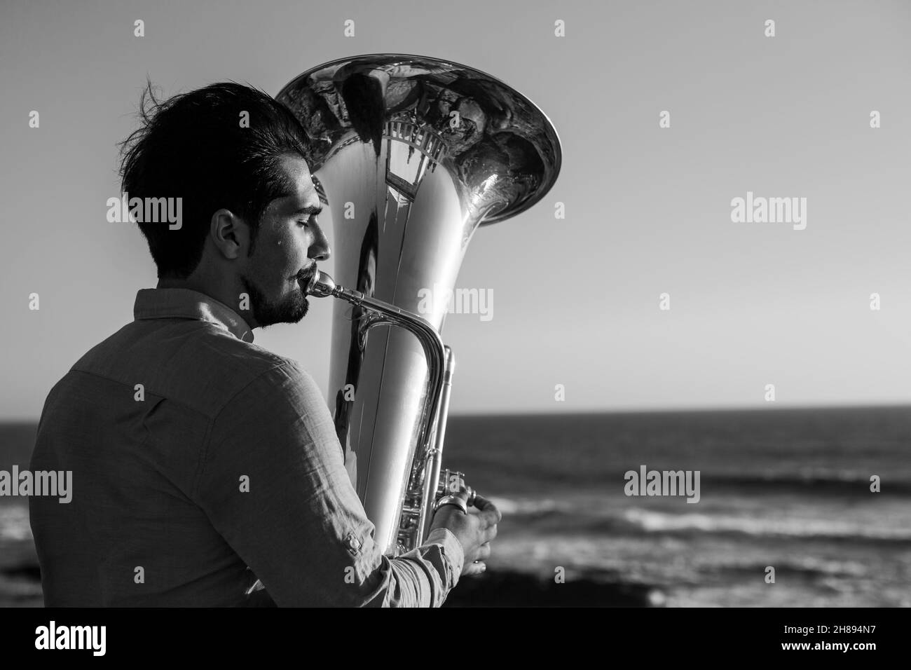 A musician plays a trumpet near the ocean. Black and white photo. Stock Photo