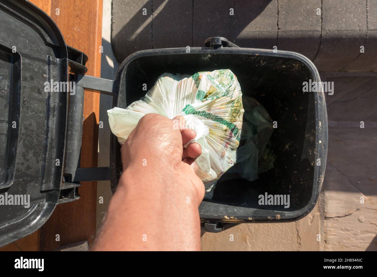 Adult male dropping a bio degradable bag of food waste into a food caddy bin Stock Photo