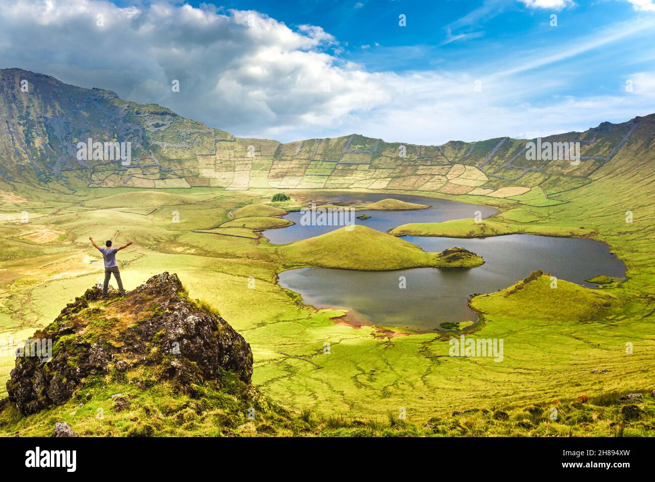 The landscape of Corvo Island in the Azores with man on rock peak with open arms. Concept of freedom and travel adventure. Stock Photo