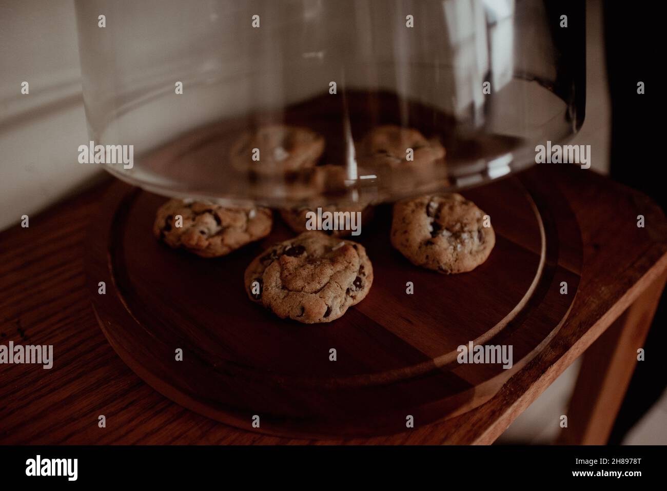 Lifting glass pastry display to reveal freshly baked homemade salted chocolate chip cookies. Moody hipster natural lighting on cookies, pastries Stock Photo
