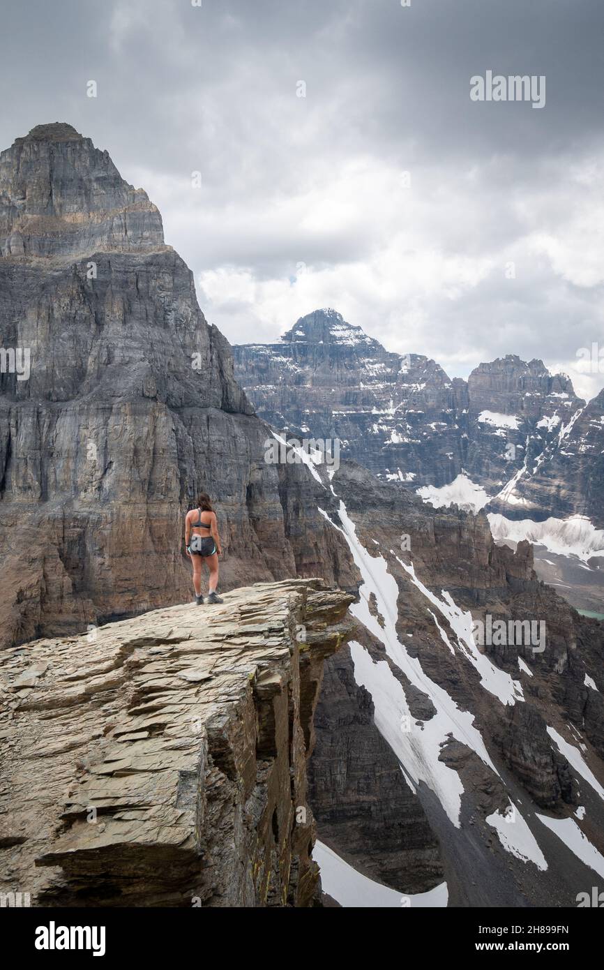 Female hiker standing on the edge of cliff, surrounded by mountains, Canadian Rockies, Canada Stock Photo