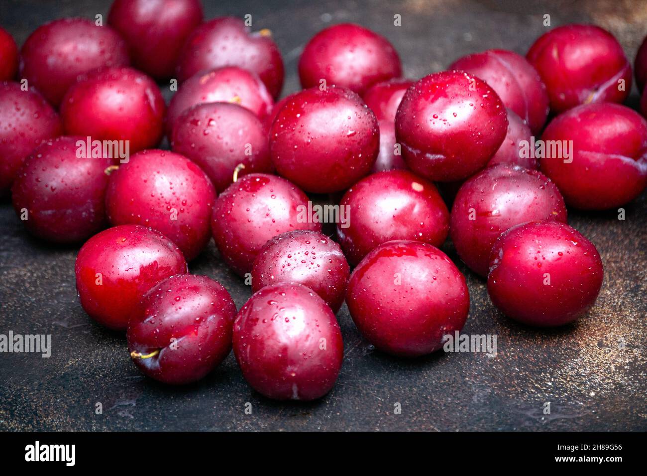 Burgundy plums are scattered on the table in droplets of water Stock