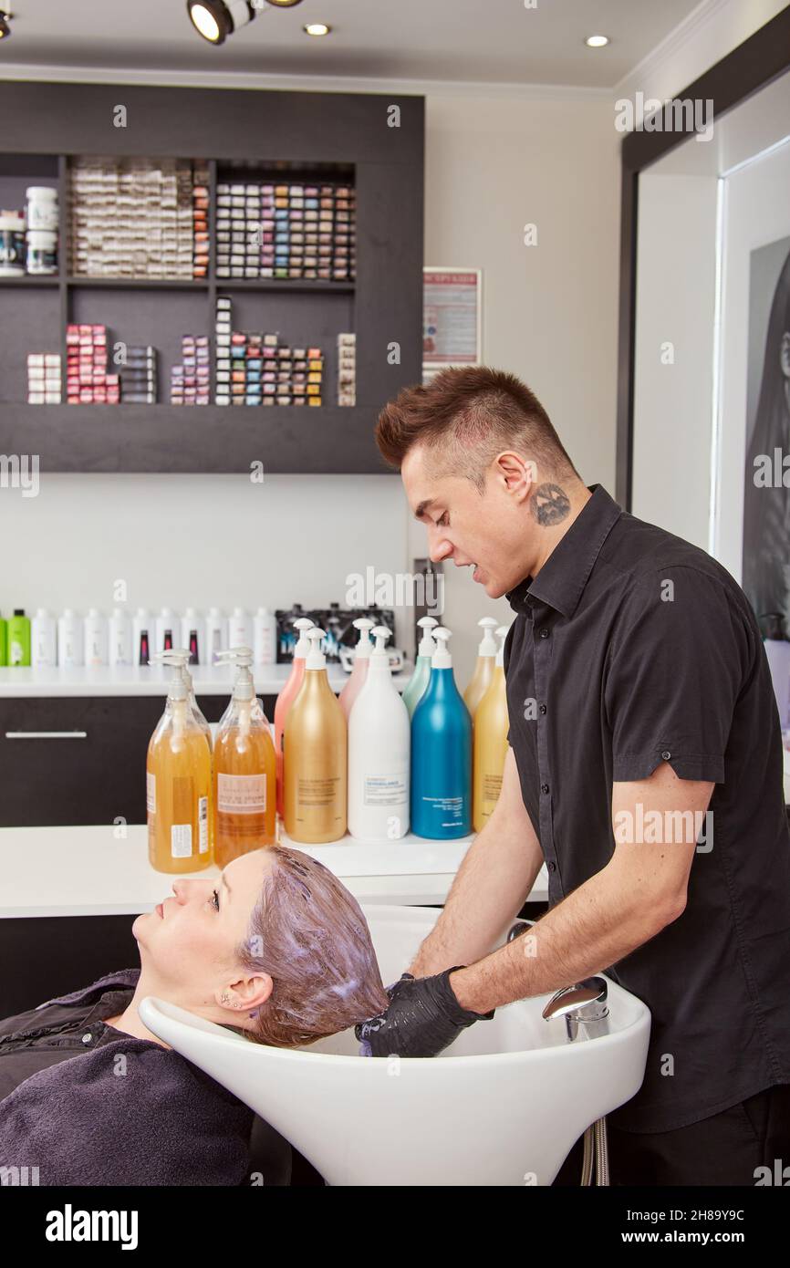 Handsome hairdresser toning client hair in salon Stock Photo