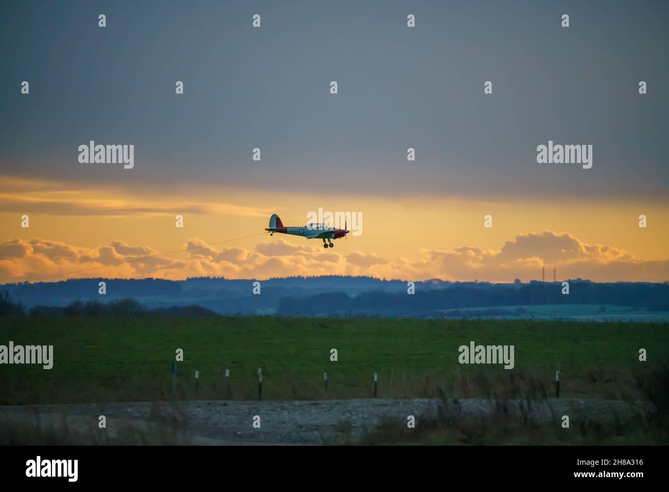 a 1950s De Havilland DHC-1 Chipmunk approaches landing with sunset background, on to a grass runway at Netheravon Airfield, Wiltshire UK Stock Photo