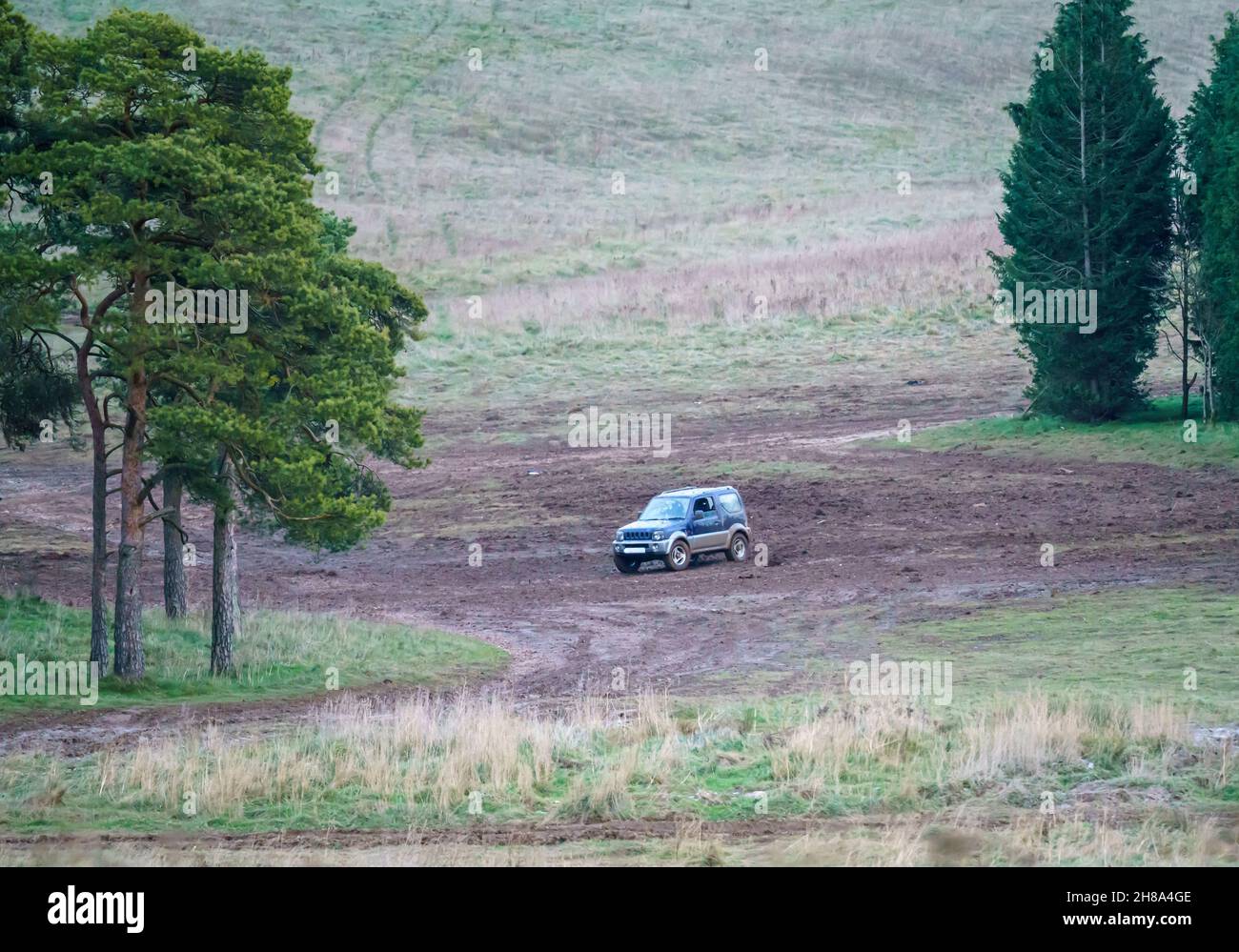 blue and silver Suzuki Jimny 4x4 off-road vehicle driven around a muddy expanse in woodland, Wiltshire UK Stock Photo