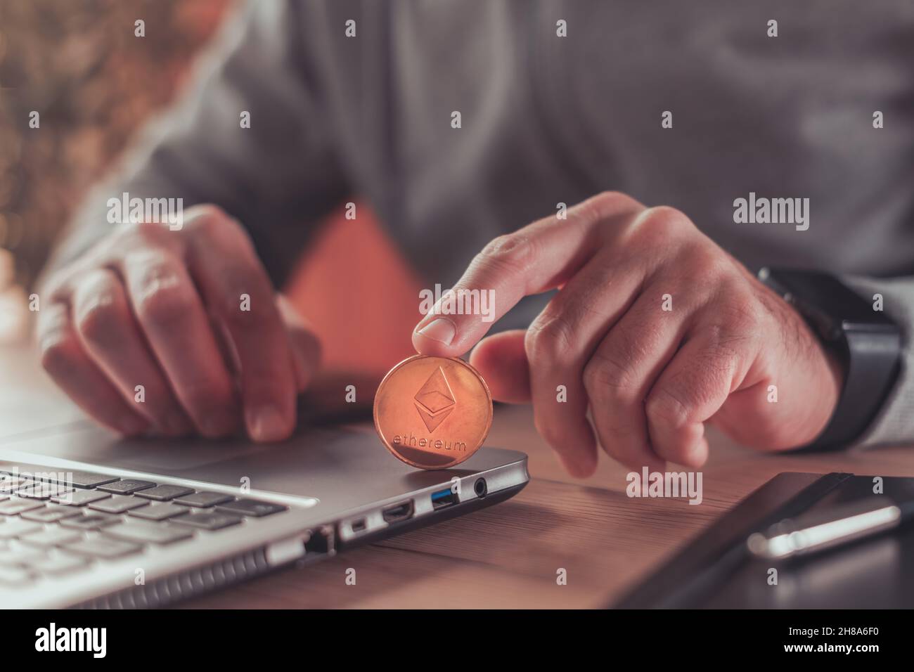 Entrepreneur trading with Ethereum cryptocurrency, conceptual image of male  person holding golden coin in front of laptop computer Stock Photo - Alamy