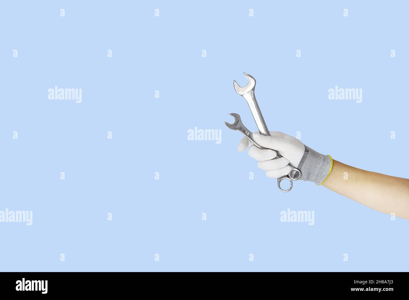Gloved hands holding wrench, spanner construction tools. Work tools on blue background Stock Photo