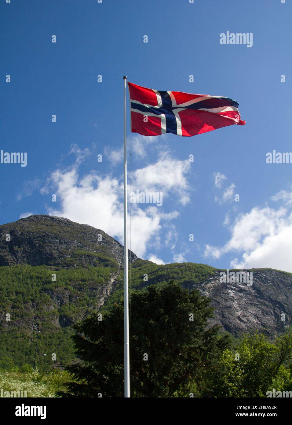Norwegian national flag in the breeze against a blue sky with mountain ...