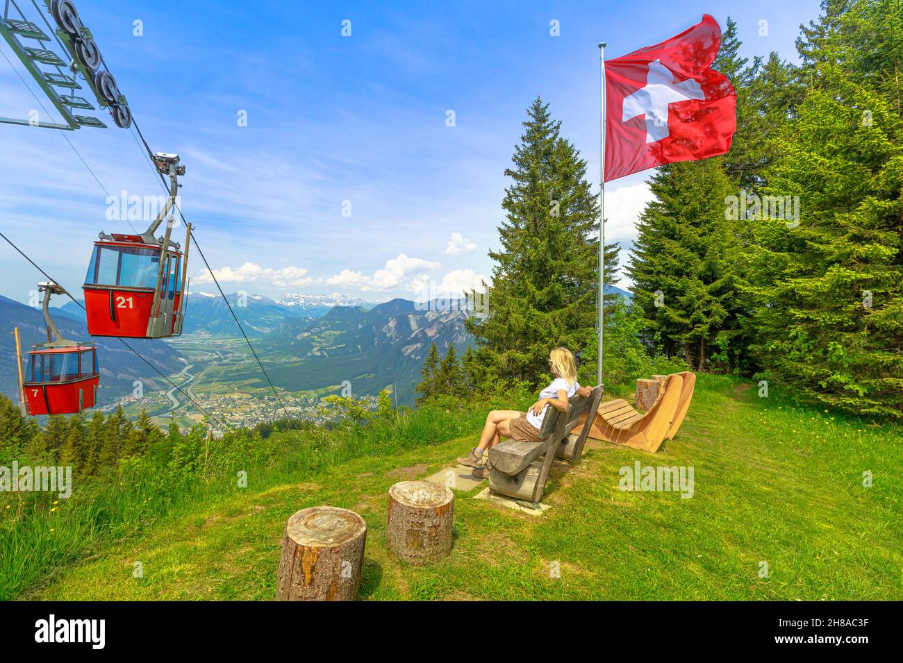 Red cable car cabin from Chur to Kanzeli and Brambruesch in Switzerland. Woman relaxing on top of Brambruesch. Swiss cable car of Chur or Coira with Stock Photo