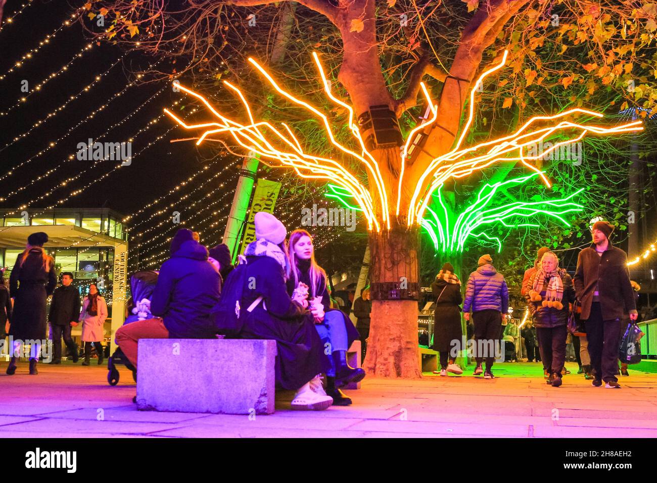 London, UK. 28th Nov, 2021. Londoners sit and stroll along the neon illuminated tree canopies that are part of the Southbank Winter Lights this year. The free display can be seen every day from dusk until 11.30pm, until January 9th, 2022. Credit: Imageplotter/Alamy Live News Stock Photo