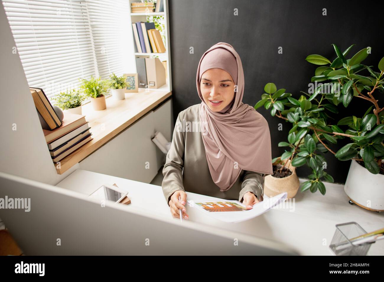 Successful young teacher in hijab looking at computer screen during ...