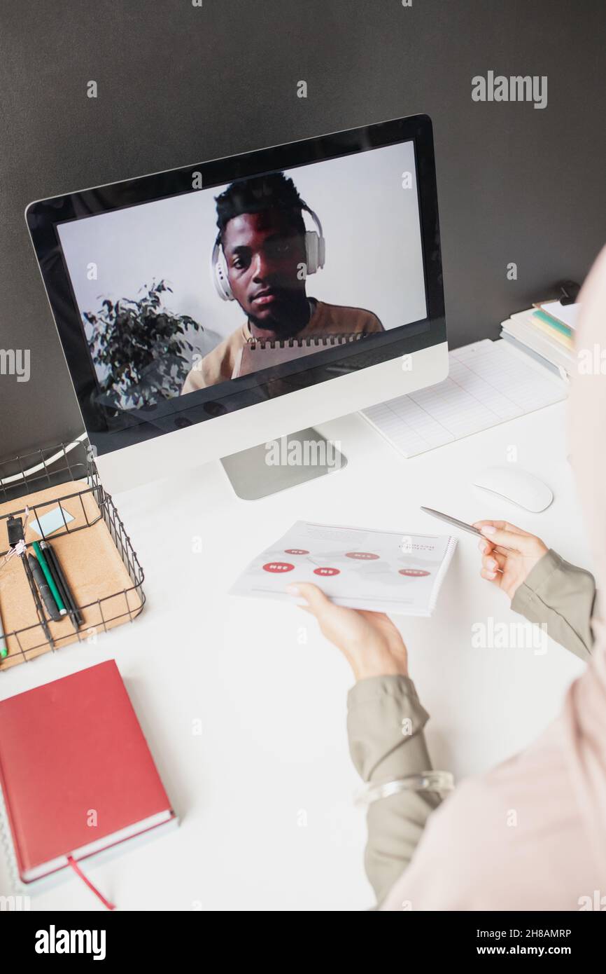 African guy with headphones on computer screen looking at teacher explaining data on paper during online lesson Stock Photo