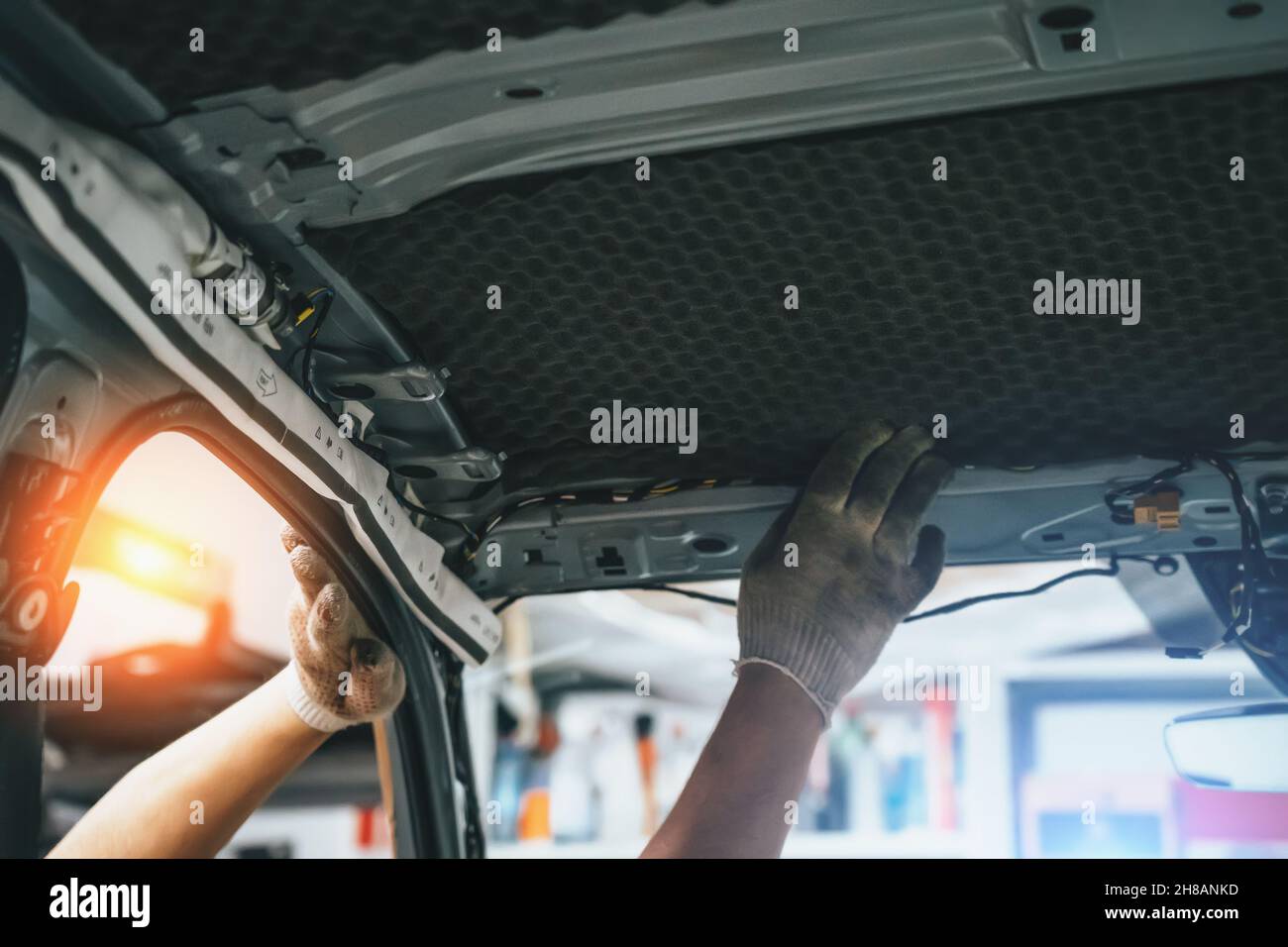 Worker hands glues soundproofing material to inside of car roof