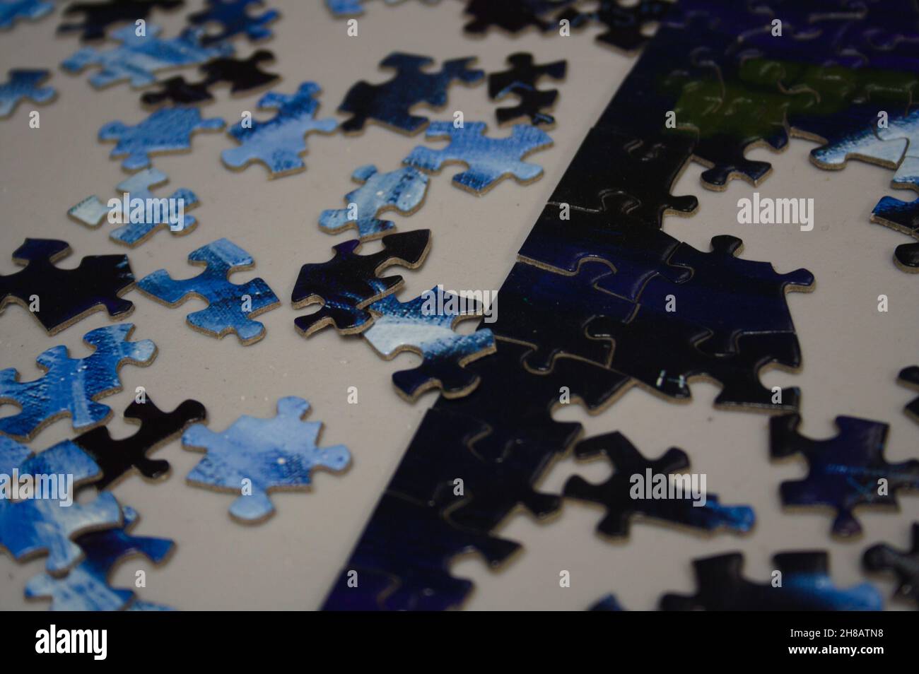 Deep blue and white center pieces of an unfinished puzzle are scattered across a table near the finished border. Stock Photo