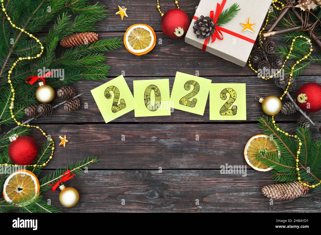 Happy New Year 2022. Yellow sticky notes with numbers 2022 on a festive wooden background with copy space. Flat lay composition with gift box, fir bra Stock Photo