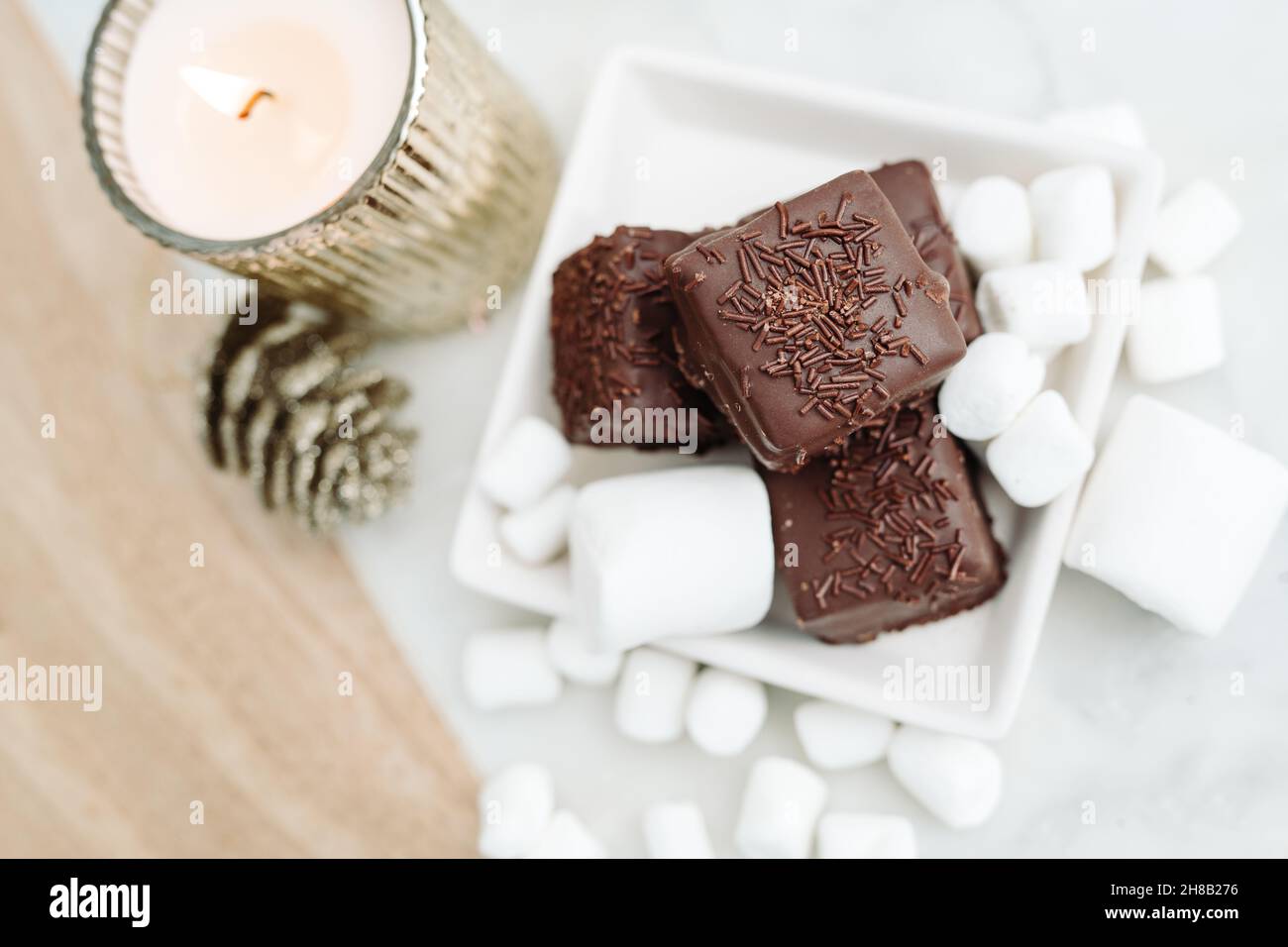 Dark Chocolate Petit Fours on White Background with Marshmallows, Candle Flat Lay Stock Photo
