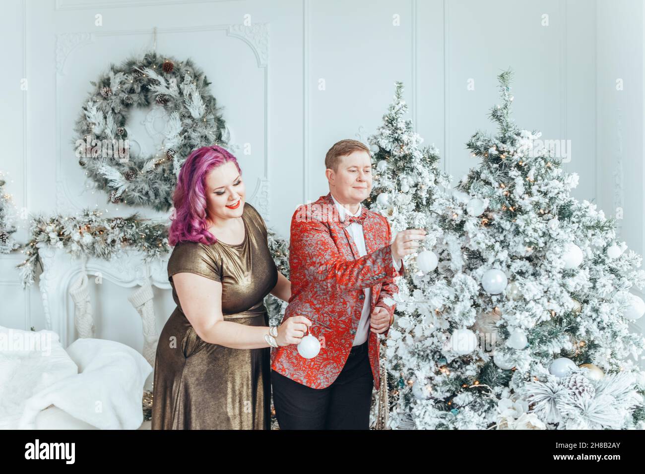 LGBTQ lesbian couple celebrating Christmas or New Year winter holiday together. Gay female lady with butch partner decorating Christmas tree at home. Stock Photo