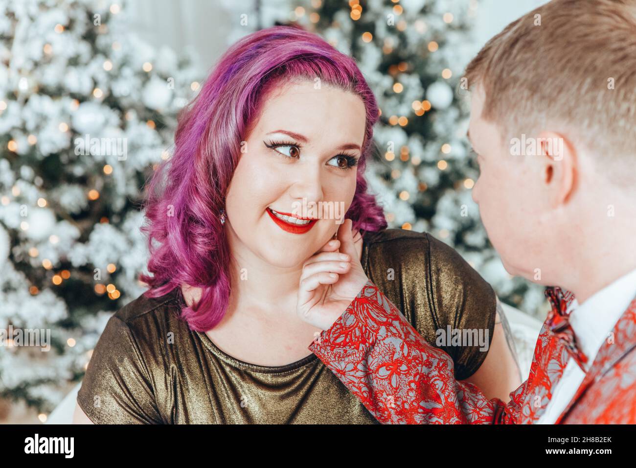 LGBTQ lesbian couple celebrating Christmas or New Year winter holiday together. Gay female lady with butch partner hugging cuddling on couch sofa at h Stock Photo