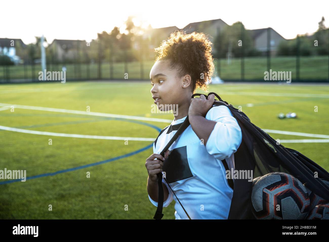 UK, Rear view of female soccer player carrying bag with balls in field Stock Photo