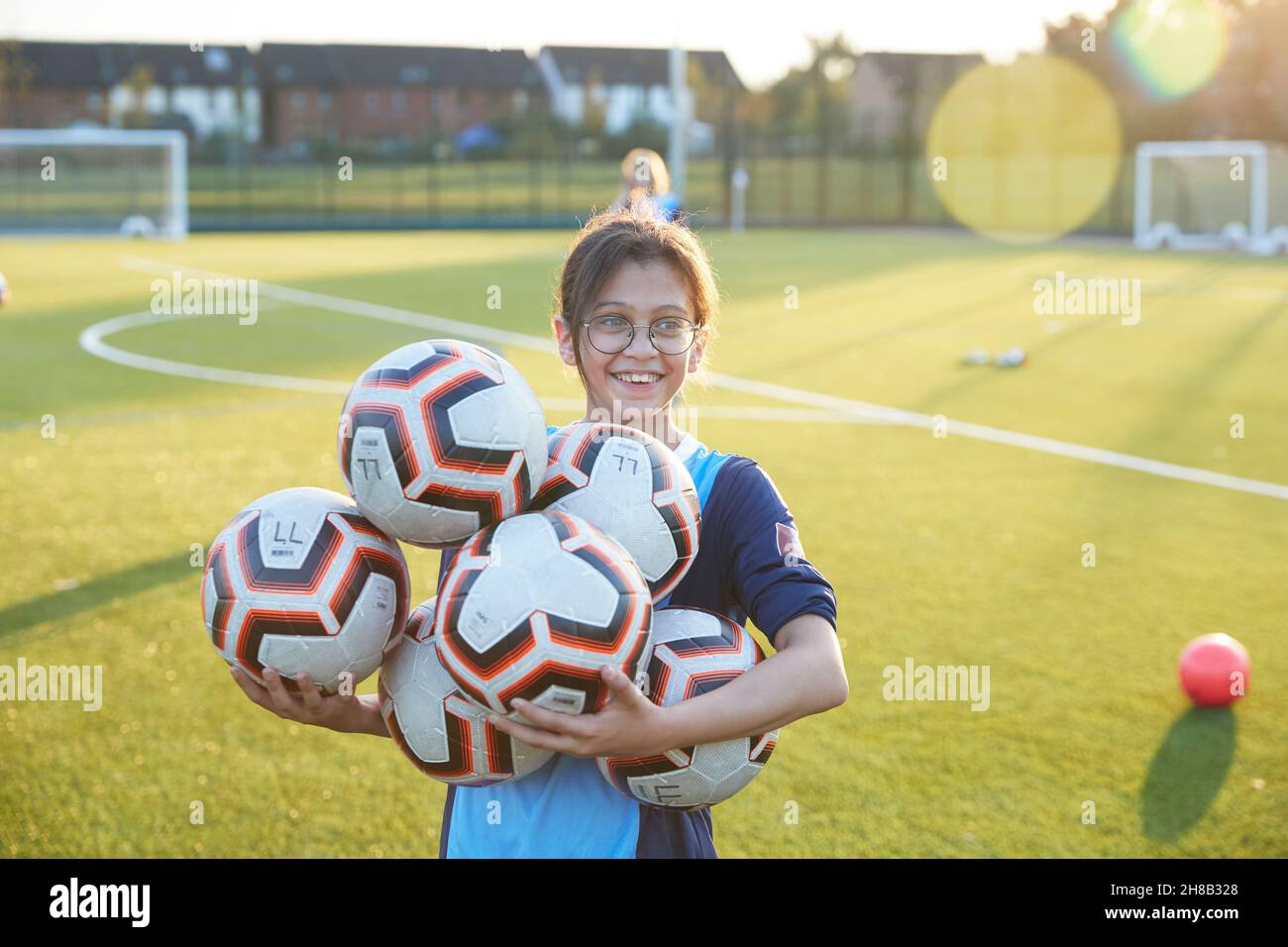 UK, Smiling female soccer player holding balls in field Stock Photo