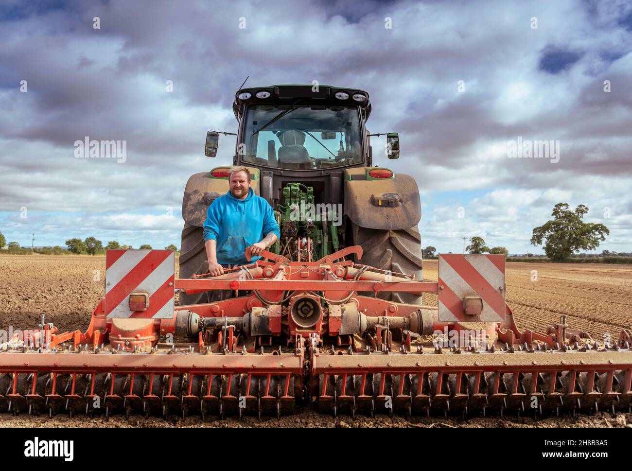 Farmer at tractor with cultivating plough in plowed field Stock Photo