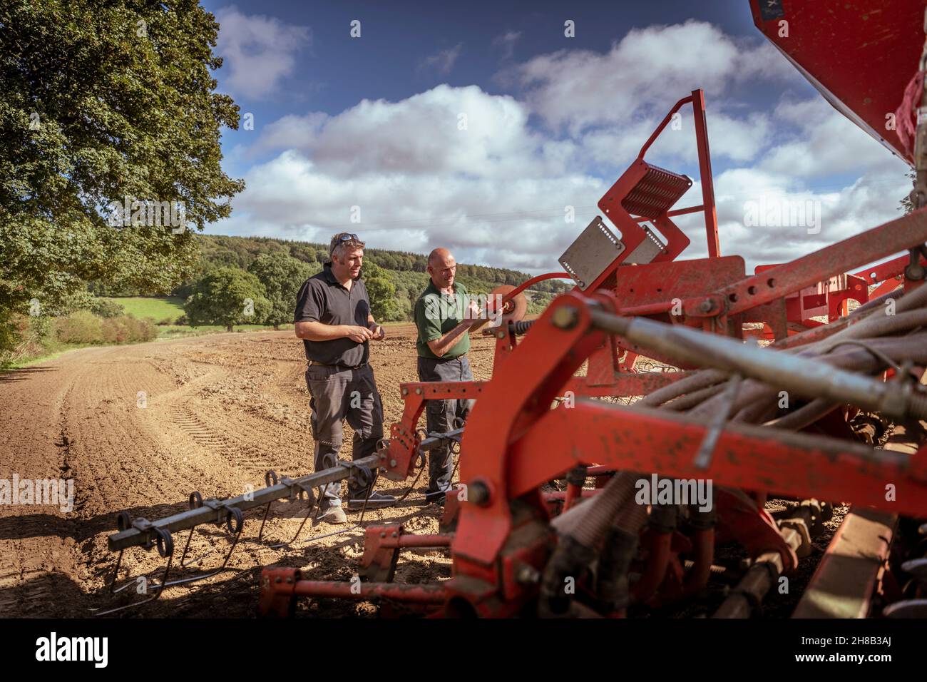 Farmers at tractor with cultivating plough in field Stock Photo