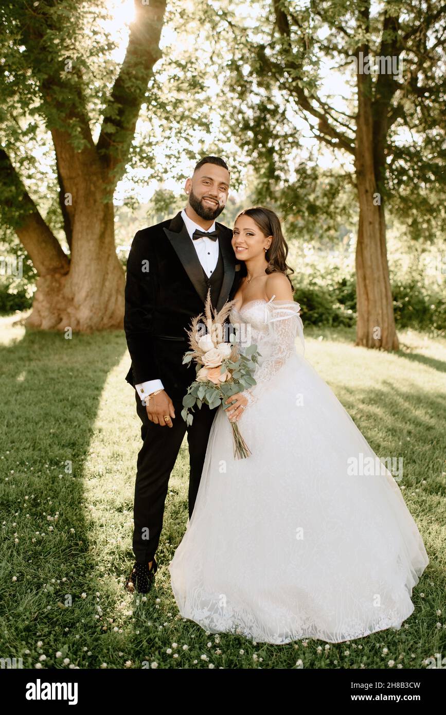Portrait of smiling bride and groom standing in park Stock Photo - Alamy