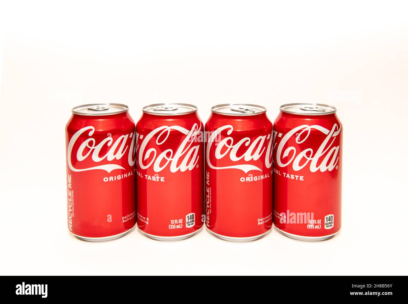 A line of four cans of Coca Cola, original taste, also known as Coke Classic, in traditional red and white cans. Stock Photo