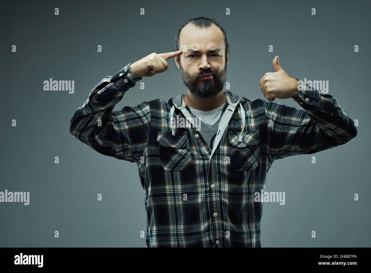 Think about it and we will succeed, trust me! - optimistic man pointing to his brain while giving a thumbs up gesture with a wry smile over a grey stu Stock Photo