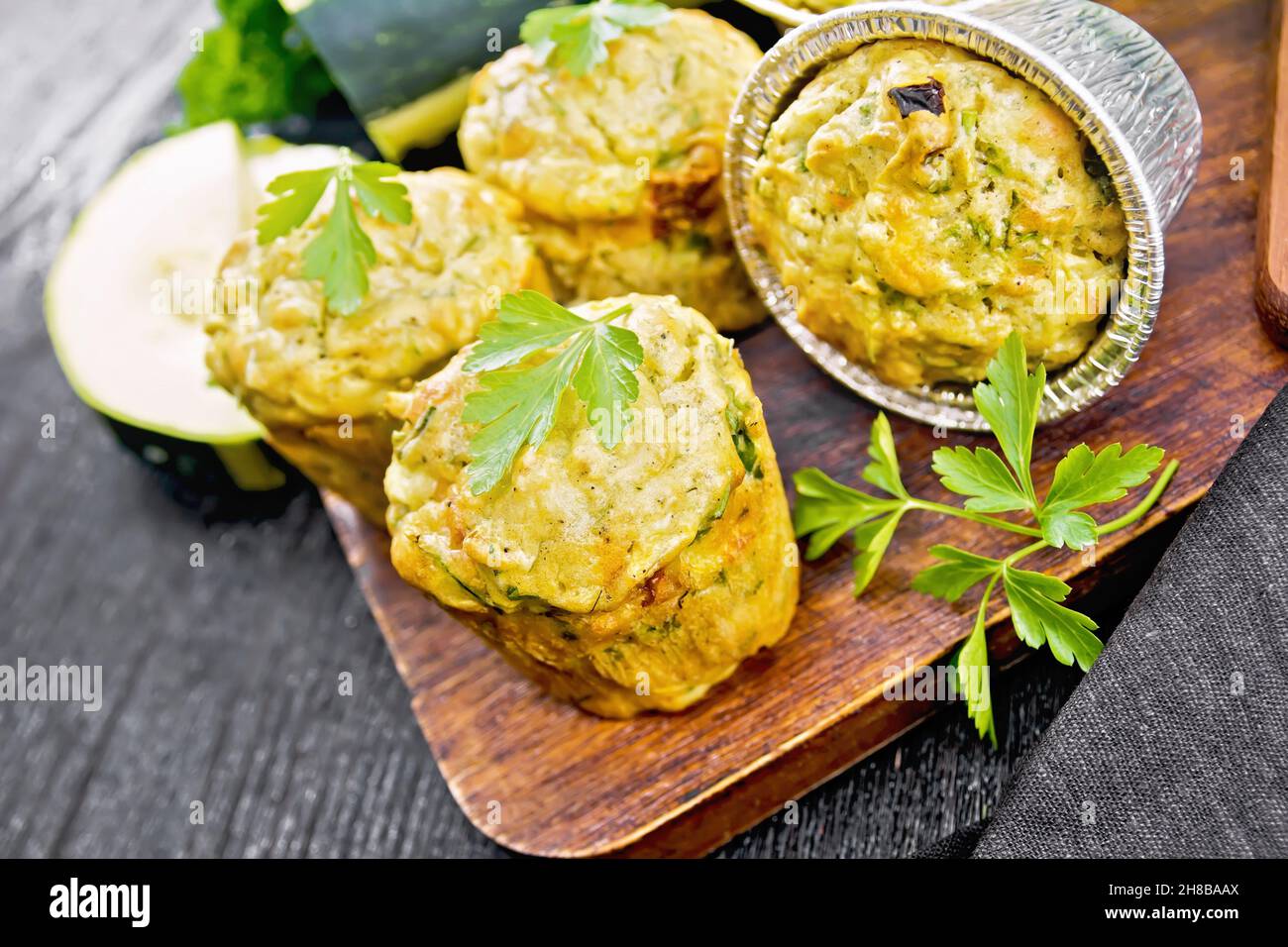 Small cheese and zucchini muffins with herbs, parsley, thyme, knife and a towel on the background of dark wooden board Stock Photo