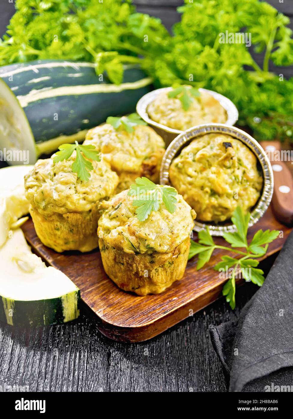 Small cheese and zucchini muffins with herbs, parsley, thyme, knife and napkin on the background of a dark wooden board Stock Photo