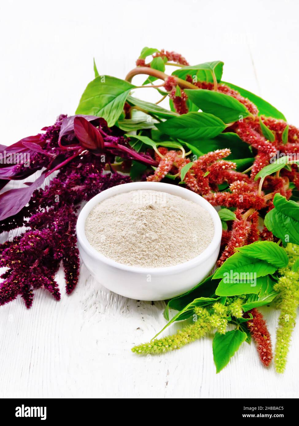 Amaranth flour in a bowl, brown, green and purple flowers of a plant on wooden board background Stock Photo