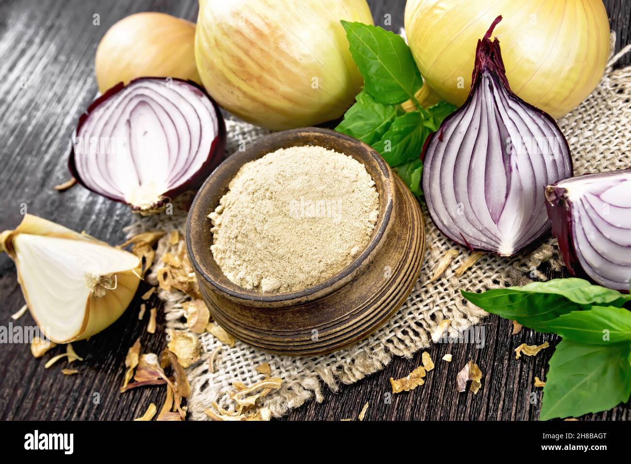 Onion powder in a bowl on sacking, purple and yellow onions, dried onion flakes and basil on wooden board background Stock Photo