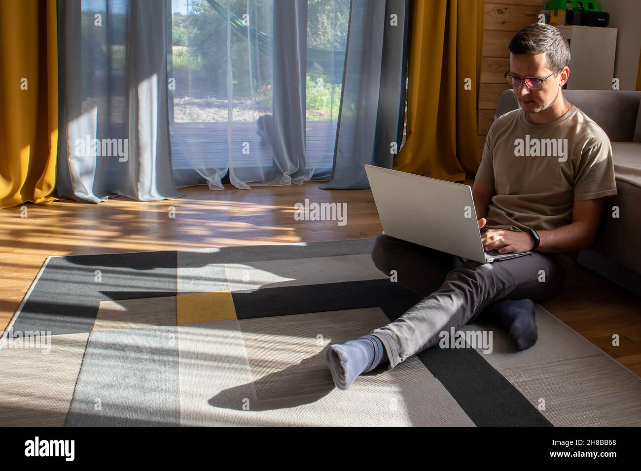 A guy in casual clothes is working on the floor in a sunny loft apartment Stock Photo