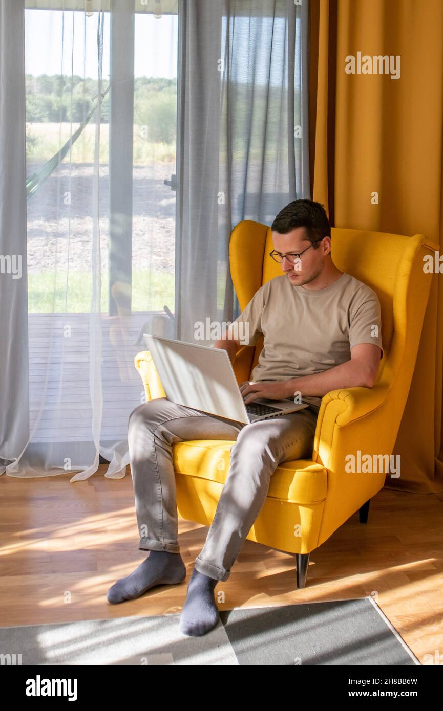 Comfortable home office. A man is sitting and working in a big yellow armchair Stock Photo