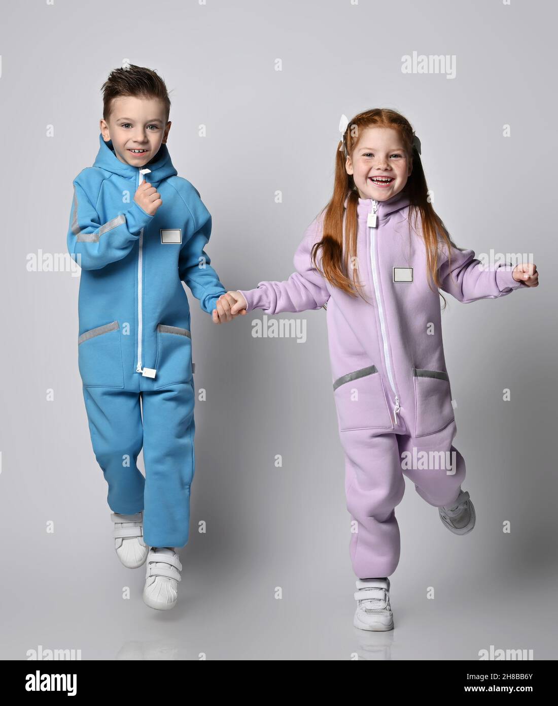 Playful kids boy and girl in blue and pink jumpsuits with zippers and pockets are jumping and having fun together Stock Photo
