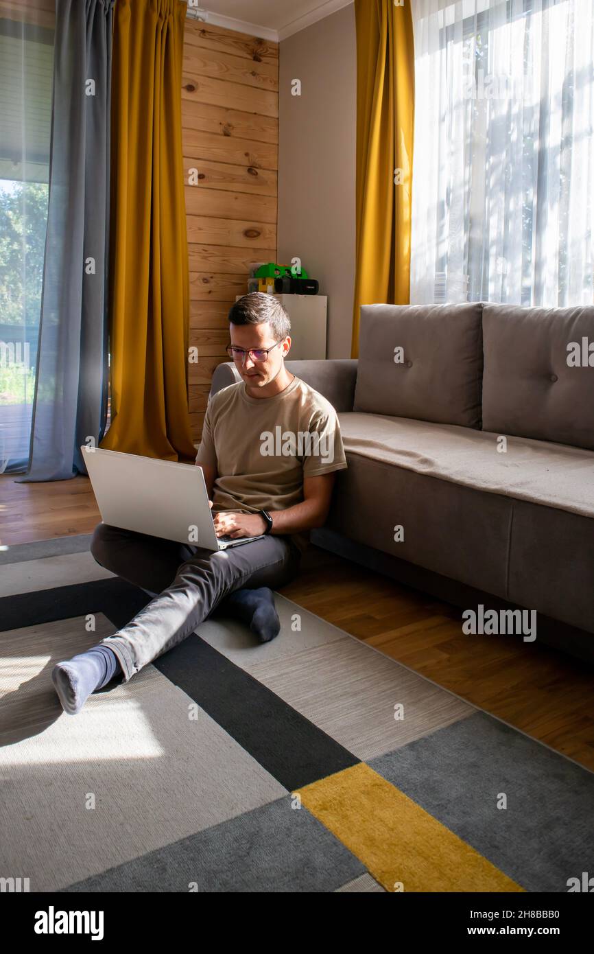 A young man with a laptop is sitting and working on the floor.  Stock Photo