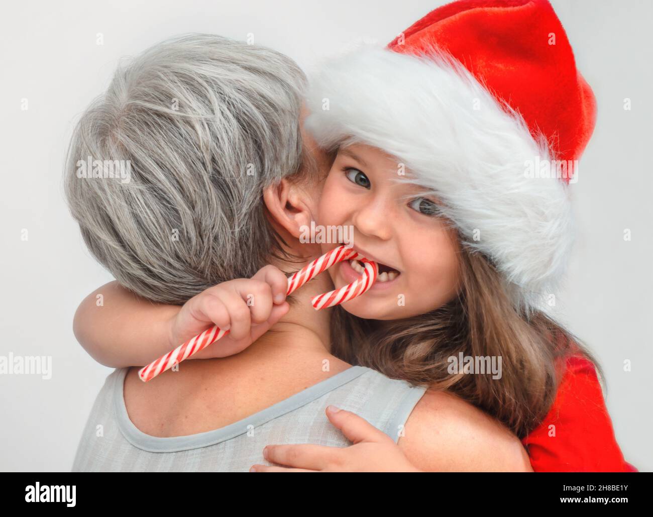 The senior hugs the child. Granddaughter eating candy cane while grandma is not looking Stock Photo