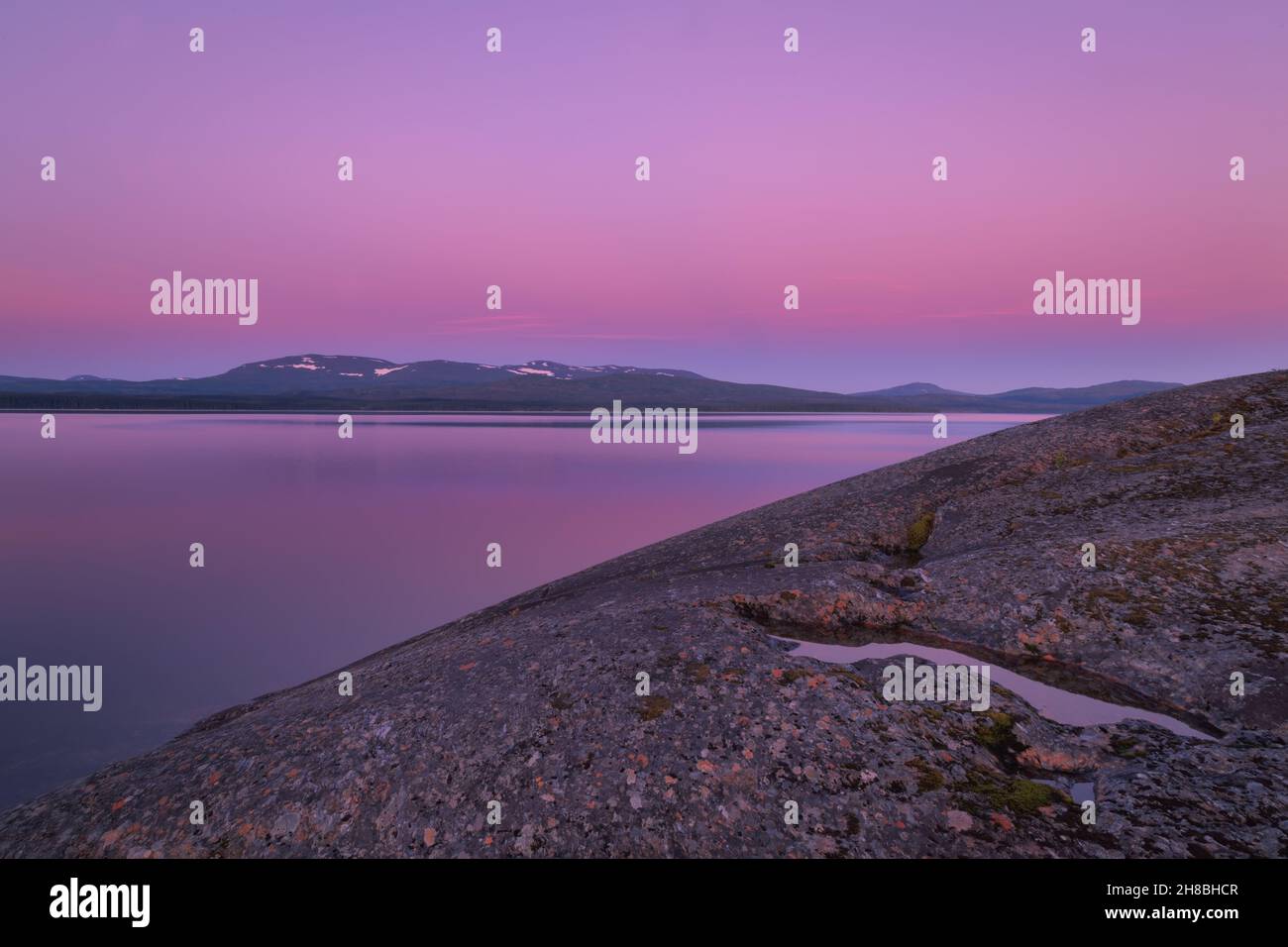 rocks in water with little snow left on mountains during sunset reflected in water Stock Photo
