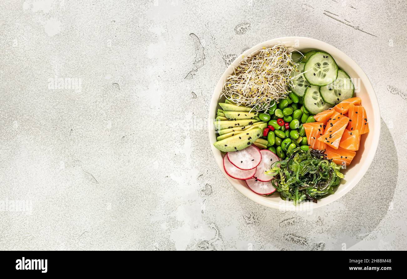 Healthy poke bowl with salmon, avocado, edamame beans, cucumber, radish, and seaweed, top view.  Stock Photo