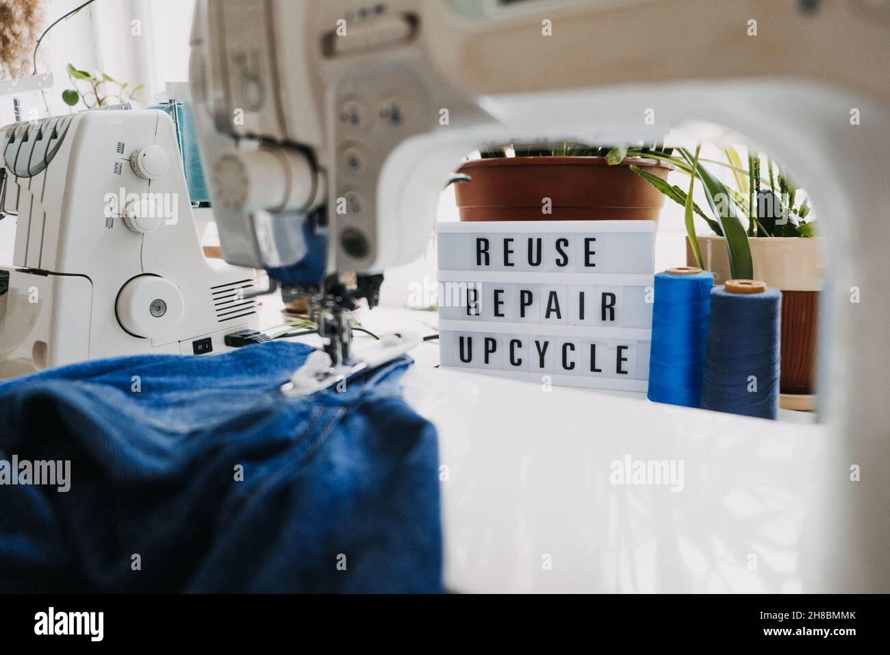 Reuse, repair, upcycle text on light board on sewing machines background. Stack of old jeans, Denim clothes, scissors, thread and sewing tools in Stock Photo
